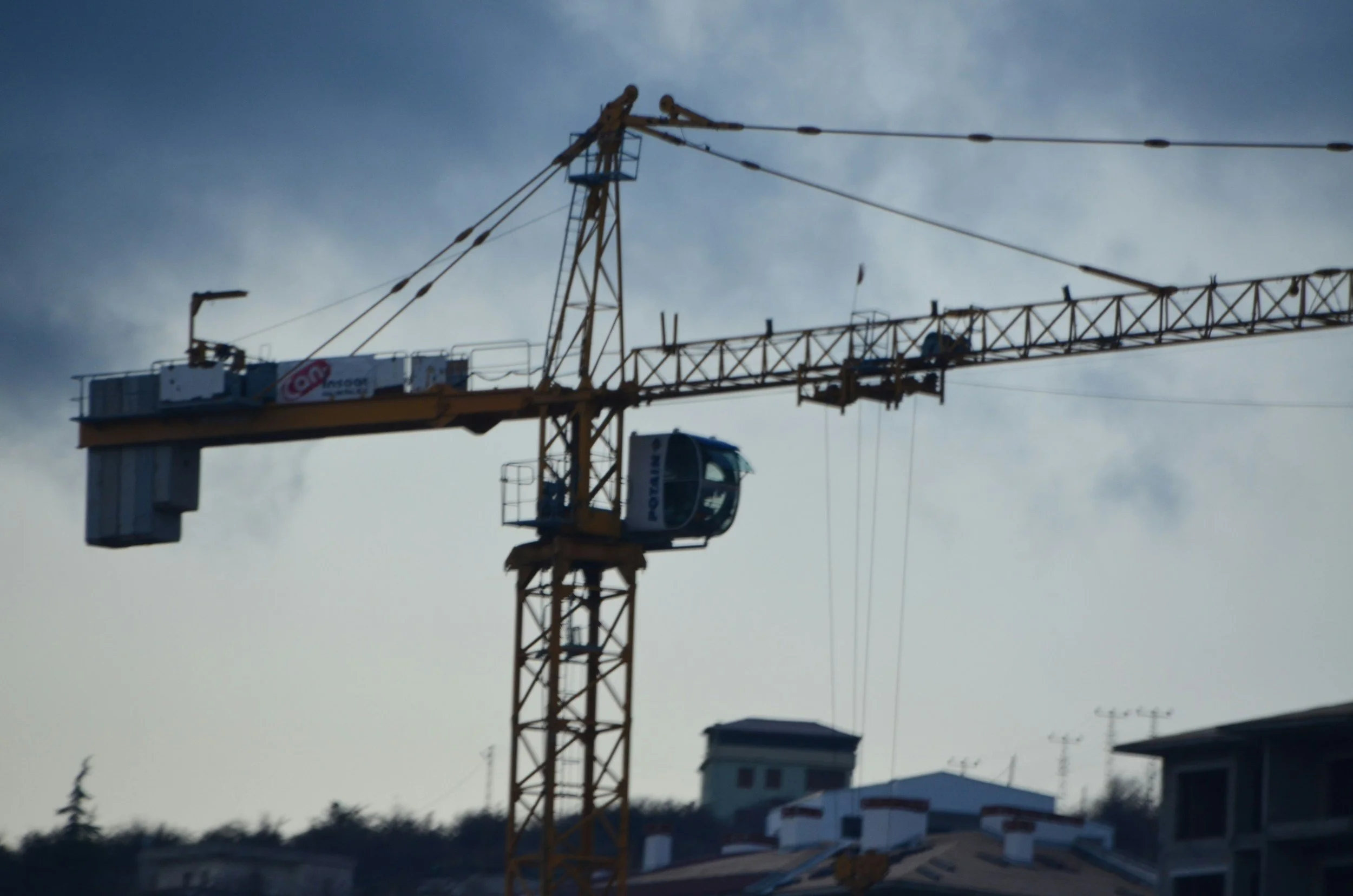 Construction crane against cloudy sky above buildings and rooftops.