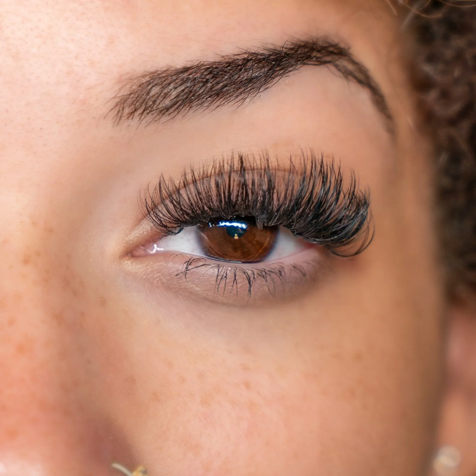 Close-up of a person's eye with long, dramatic eyelashes and brown iris.