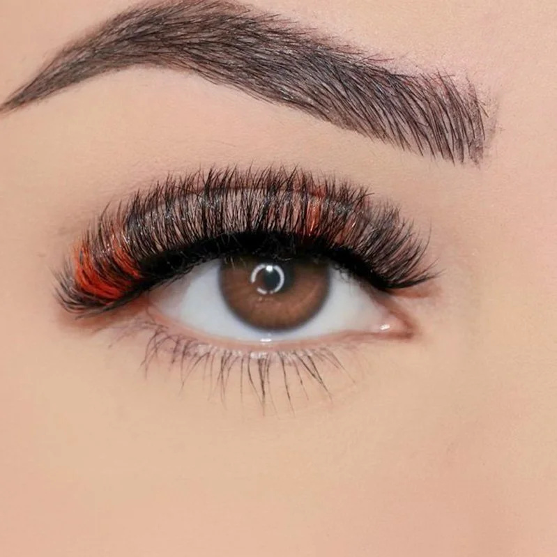 Close-up of a brown eye with makeup, including orange eyeshadow on the eyelid, false eyelashes, and a groomed eyebrow.