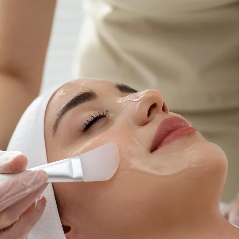 A woman receiving a facial treatment with a skincare mask applied to her face at a spa or clinic.
