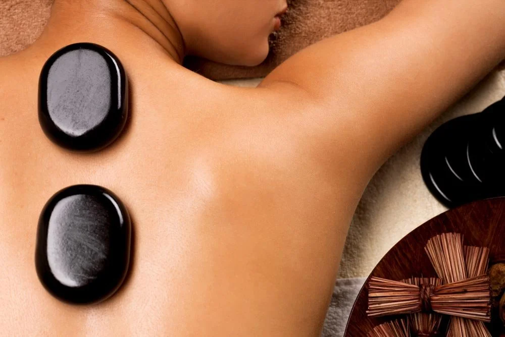 Person receiving a hot stone massage, with smooth black stones placed on their back and therapy supplies nearby.