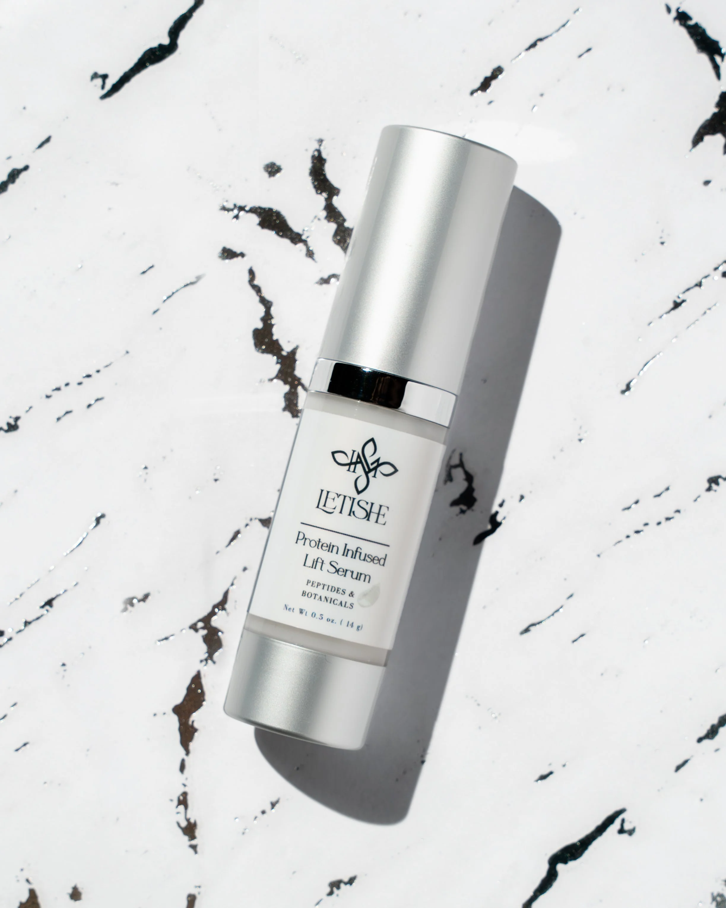 A bottle of LETISHE Protein Infused Lift Serum on a white marble surface with black veins, casting a shadow.