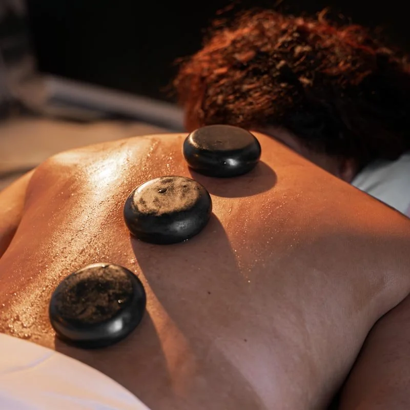 A person receiving a hot stone massage with three black stones placed on their back.