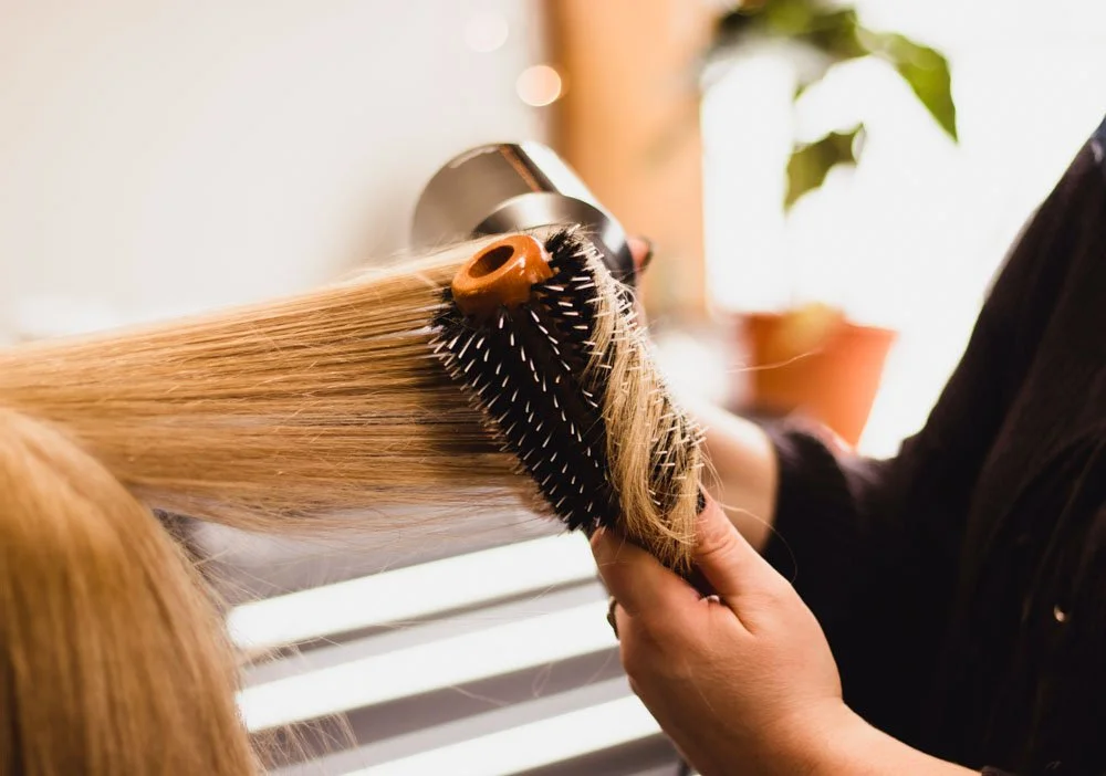 Person drying blonde hair with an airbrush hair dryer