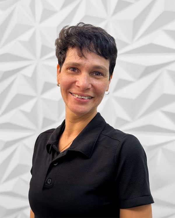 A woman with short dark hair wearing a black polo shirt, smiling, in front of a geometric patterned wall.