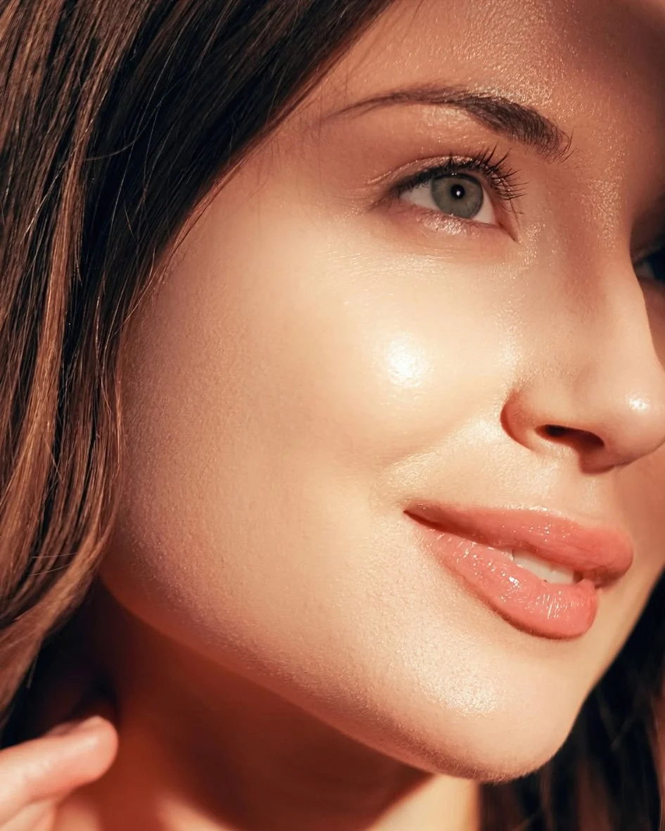 Close-up of a woman's face with smooth skin, brown hair, blue eyes, and light makeup, smiling gently.