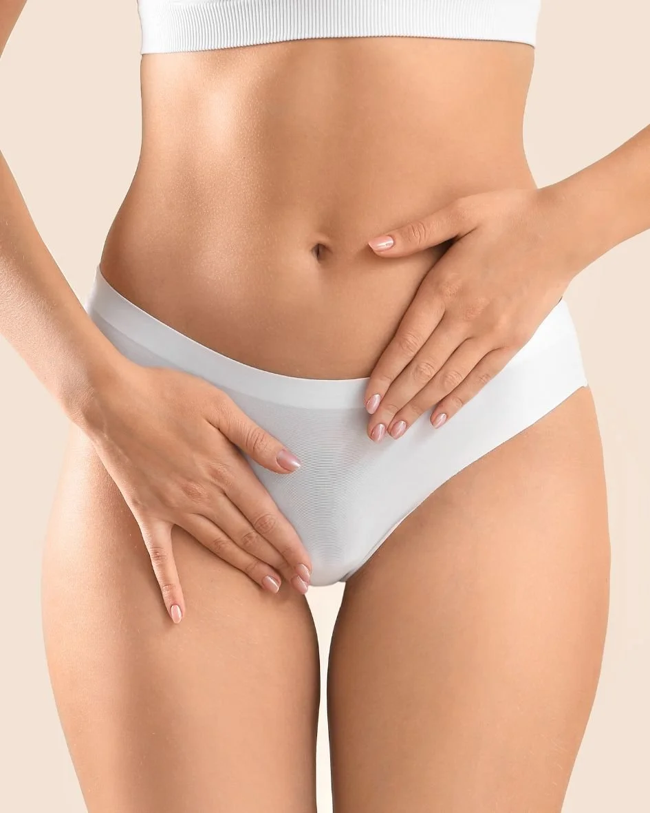 Close-up of a woman's midsection wearing white underwear, with hands resting on her hips and stomach.