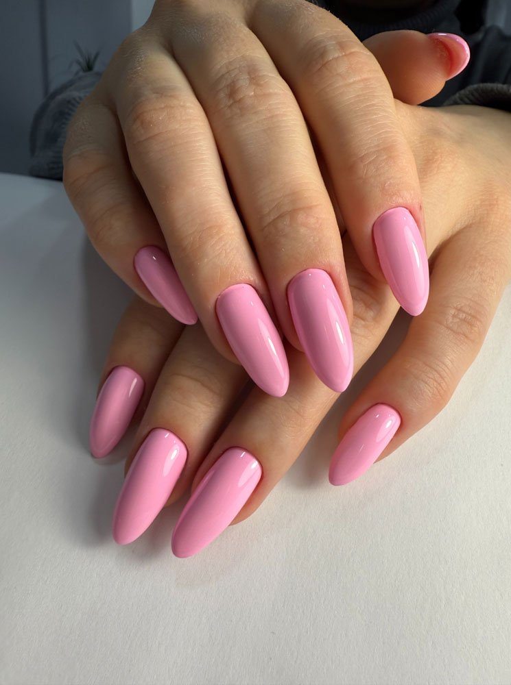 Close-up of hands with neatly manicured nails painted in light pink, resting on a white surface.