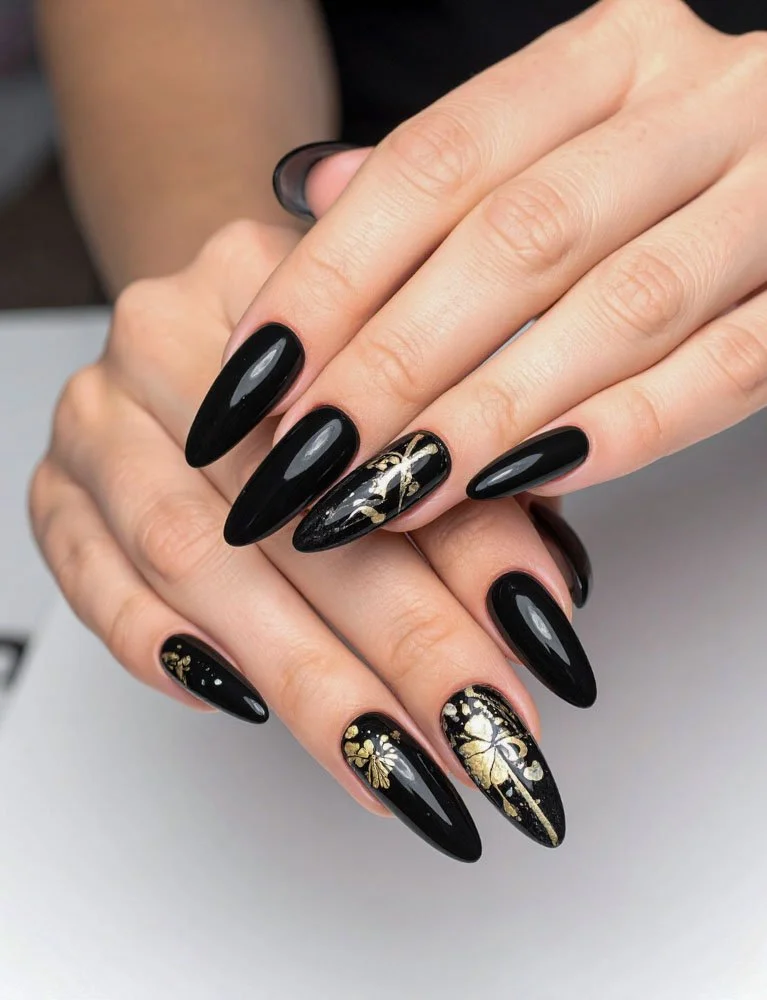 Close-up of hands with black stiletto-shaped nails with gold floral and leaf designs on some nails.