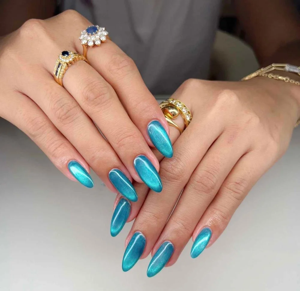 Hands with metallic blue nail polish, gold rings with gemstones, and a silver bracelet.