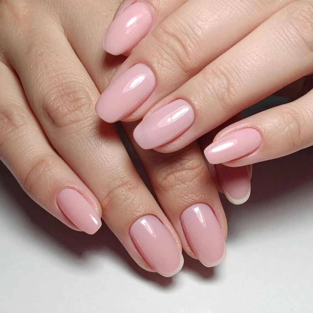 Close-up of hands with well-manicured nails painted in a light pink, glossy nail polish.