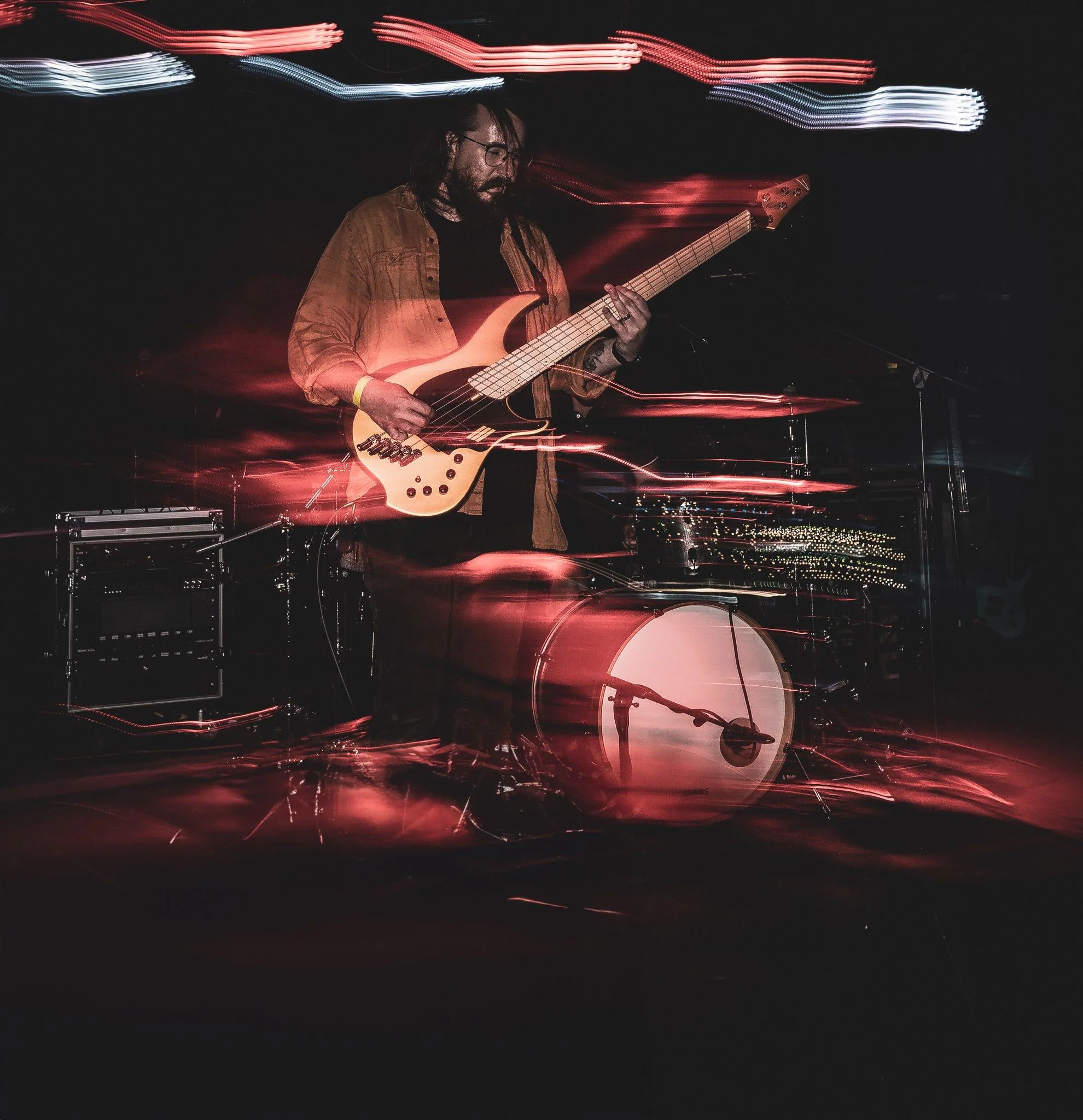 A person playing an electric bass guitar on stage with colorful light streaks in the background, creating a dynamic motion effect.