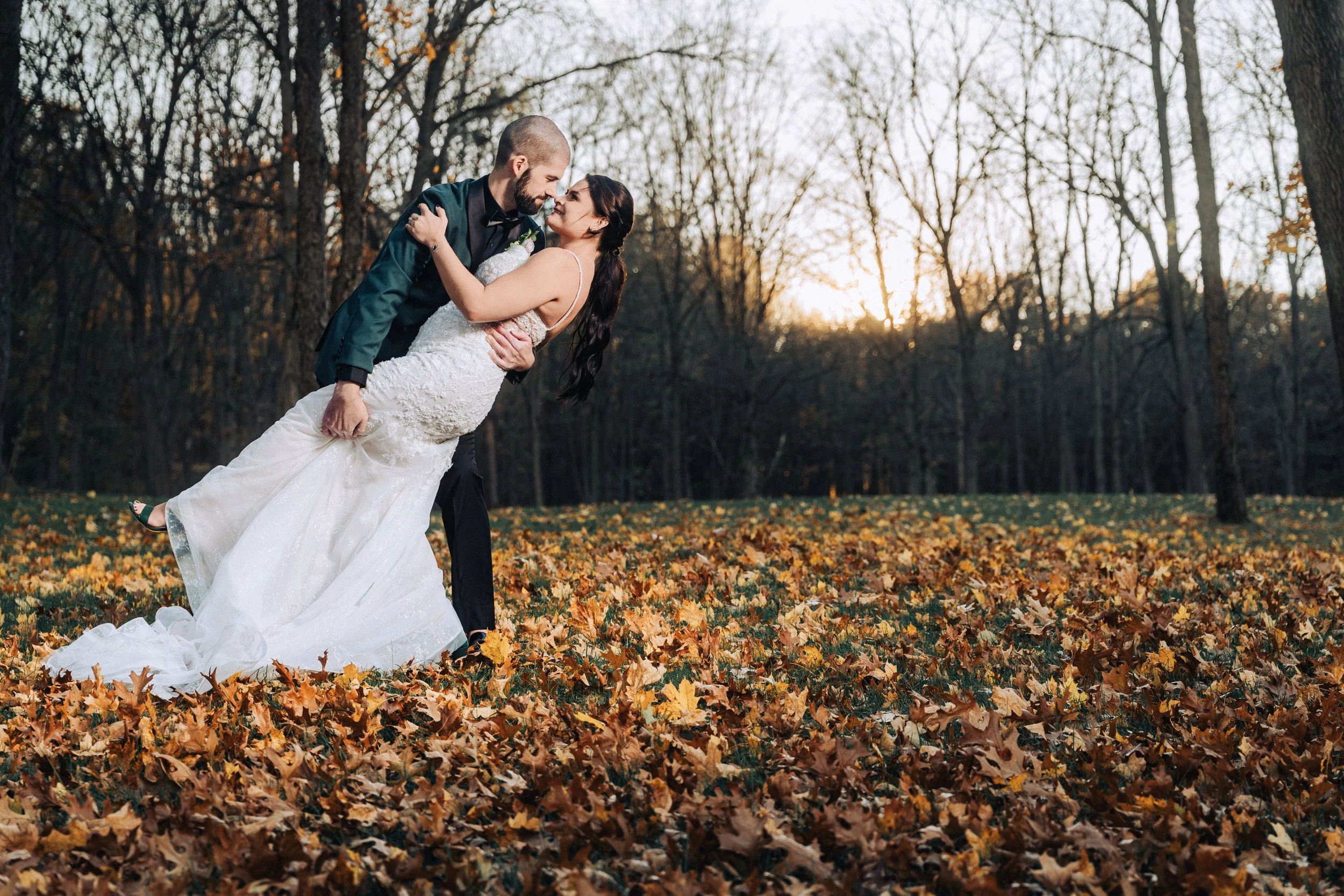Bride and groom dancing together in a field of autumn leaves during golden-hour wedding portraits.