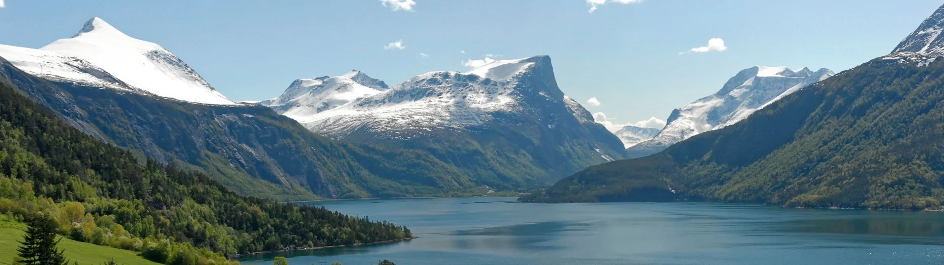 Oversiktsbilde over Eresfjord, med fjorden, grønne åssider og fjell med snødekte topper mot horisonten