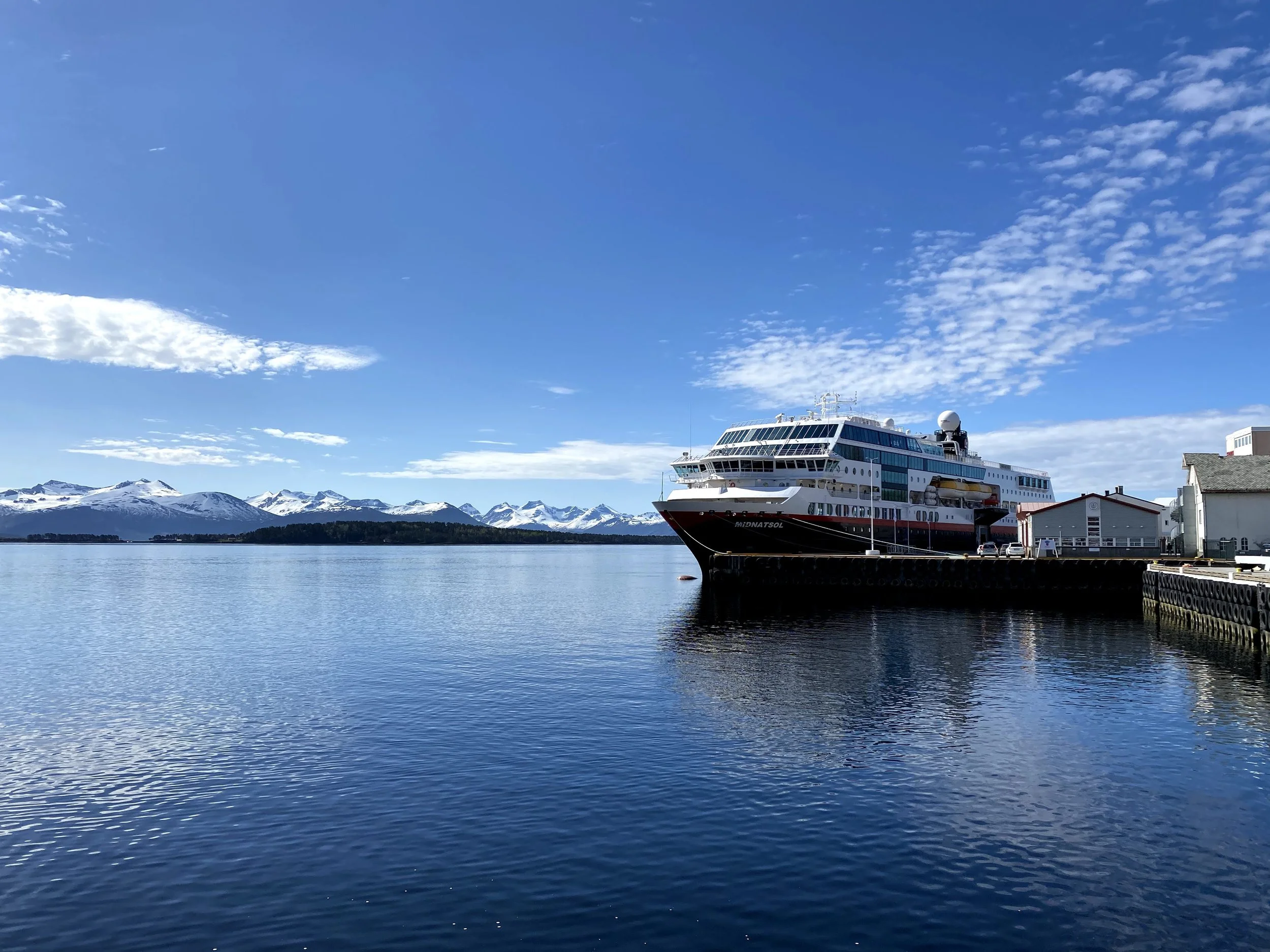 Et cruiseskip som ligger ved kai med snødekte fjell i bakgrunnen, under en klar blå himmel.
