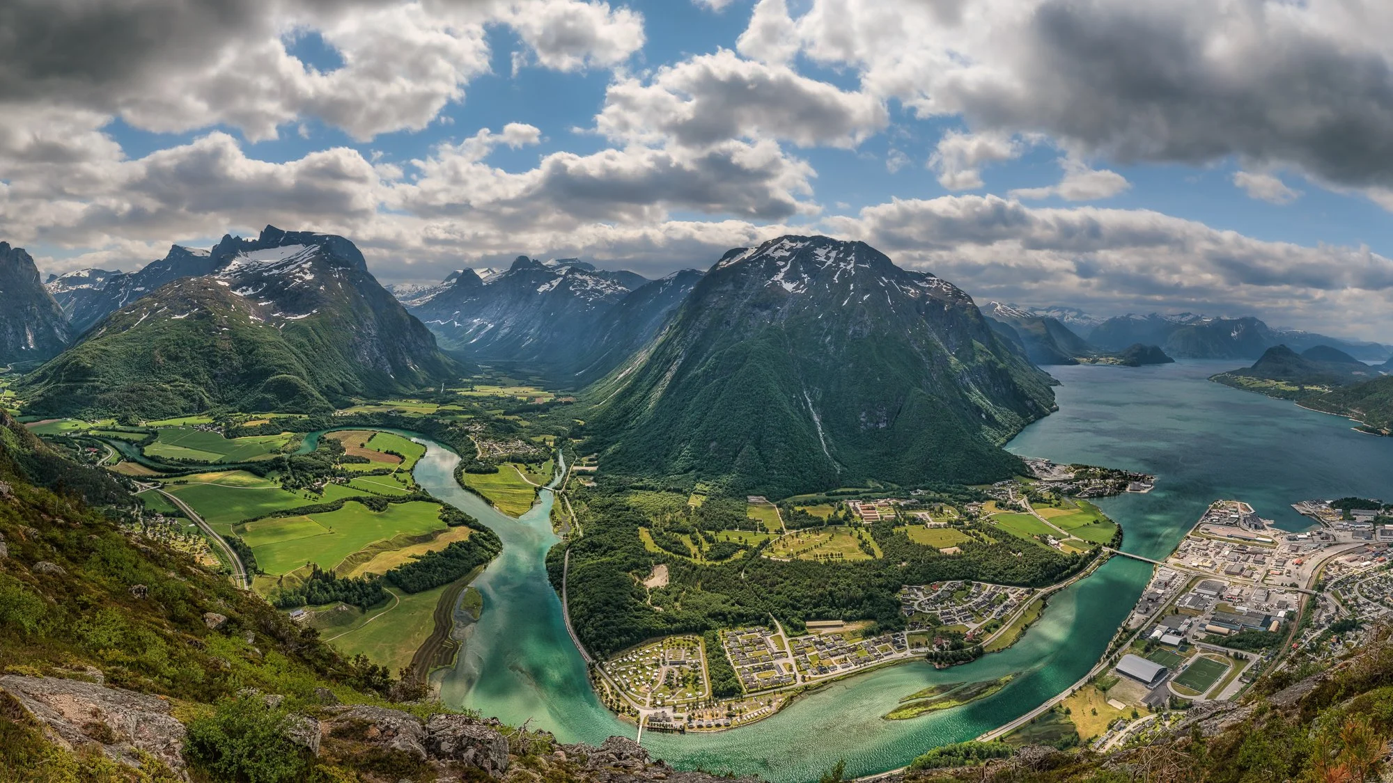 Oversiktsbilde over Åndalsnes, Rauma, med fjell, en elv som bukter seg, fjorden og lettskyet himmel