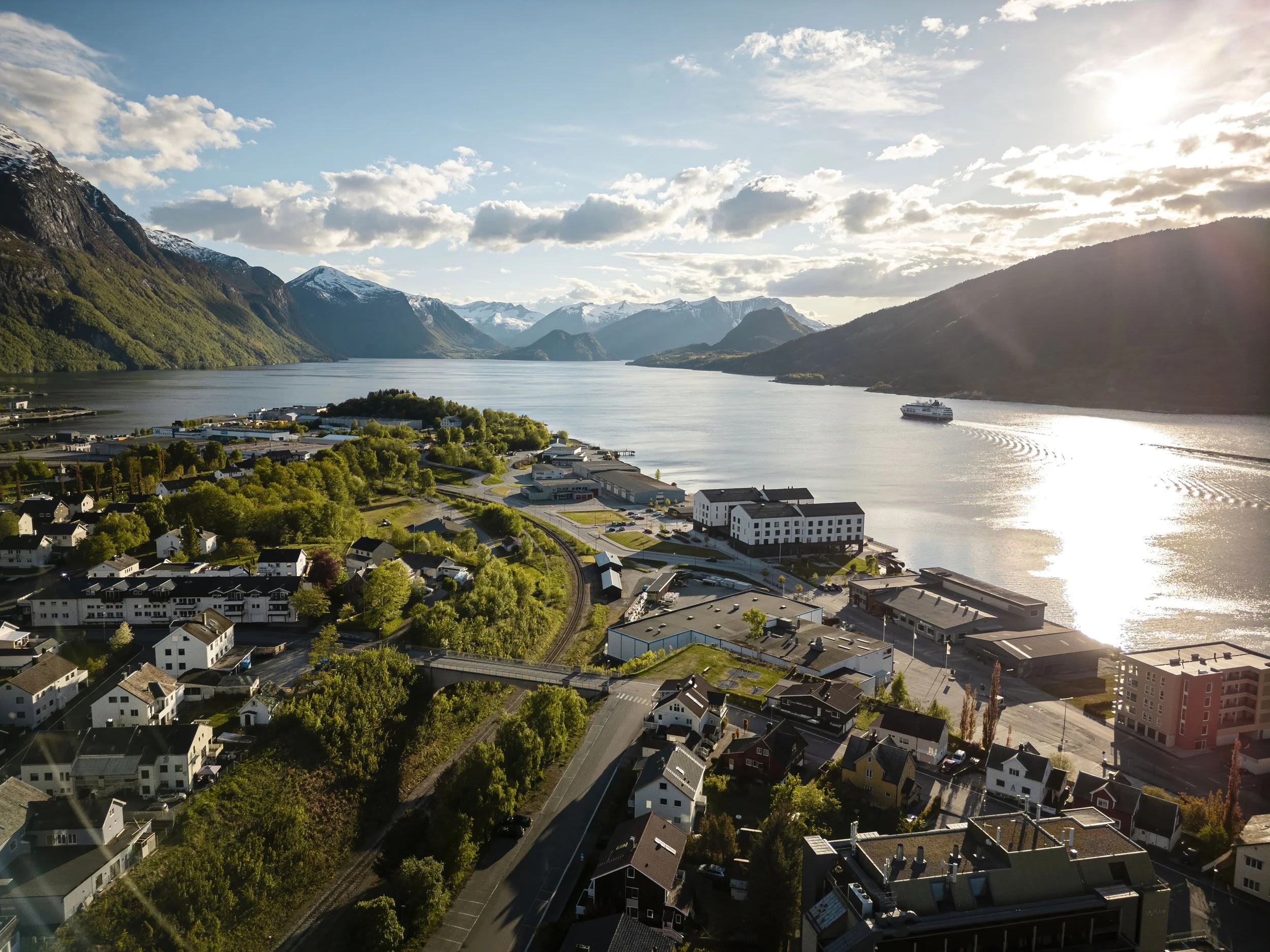 En cruisebåt på tur inn mot Tindekaia i Åndalasnes. Bildet viser Åndalsnes sentrum, med utsikt mot Torvika og utover fjorden. Det er fint vær og blå, lettskyet himmel.