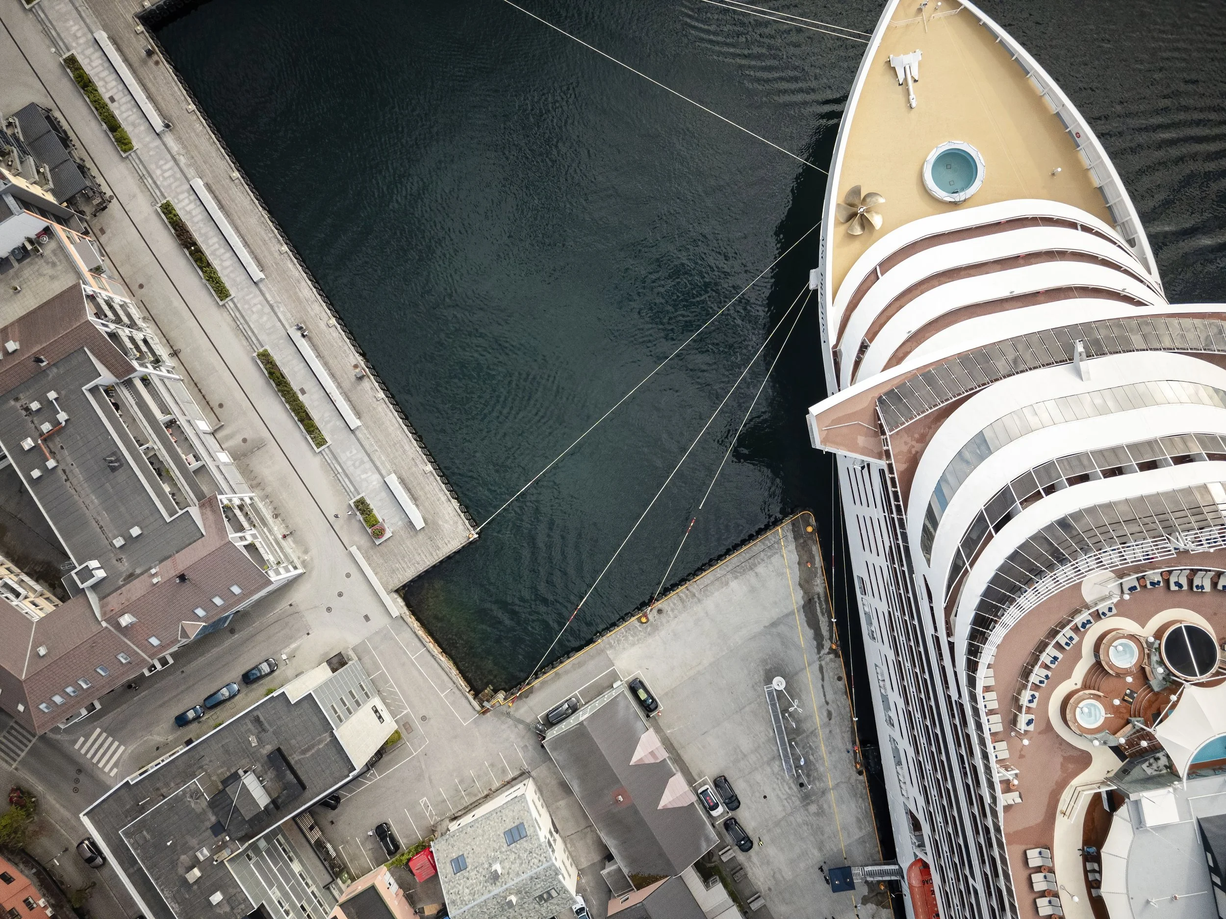 Havnen med bygninger og biler sett fra luften, med en stor cruisebåt som ligger ved kaien.