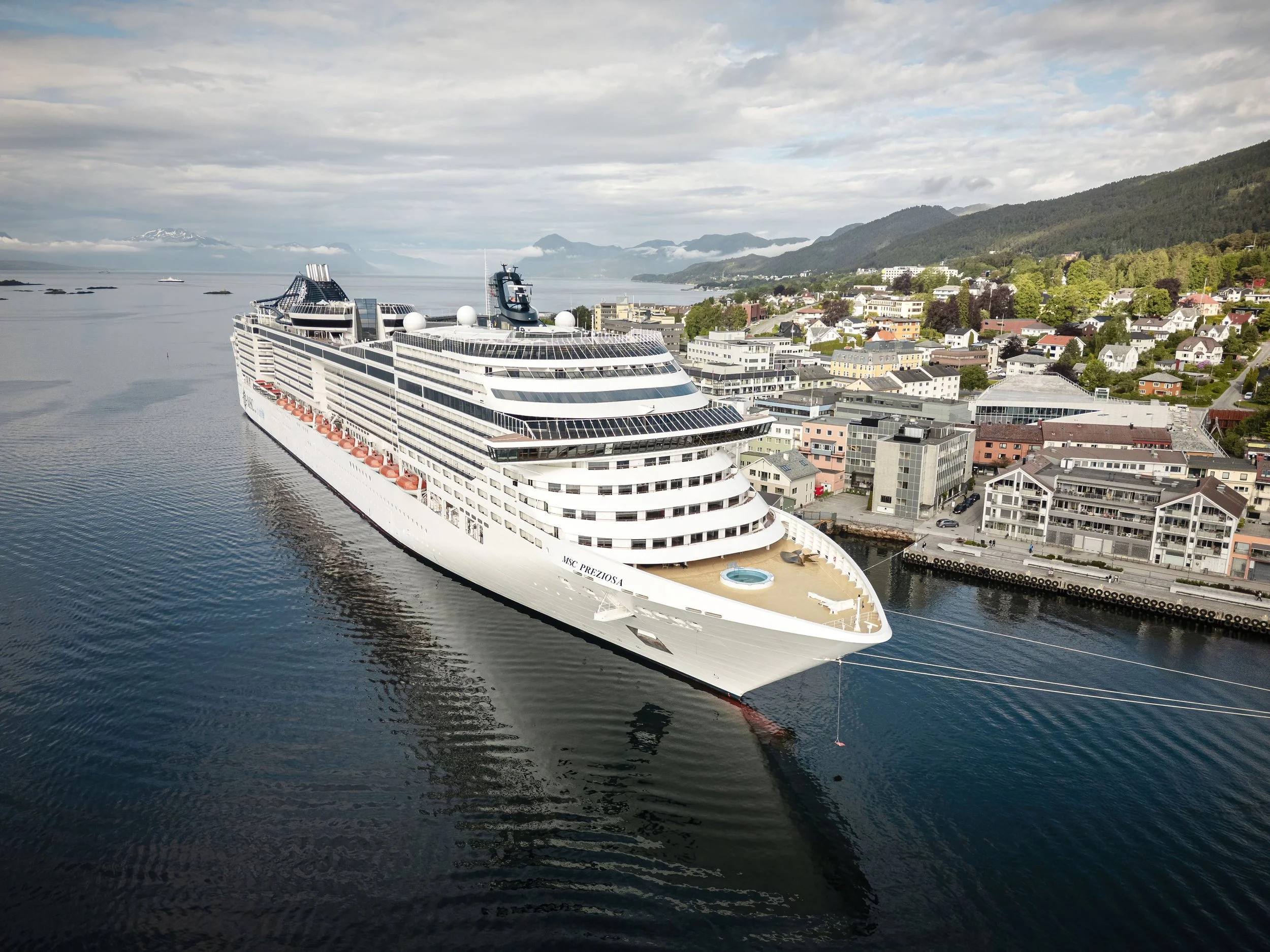 Et stort cruiseskip ved Storkaia i Molde, med en by og fjell i bakgrunnen, overskyet vær.