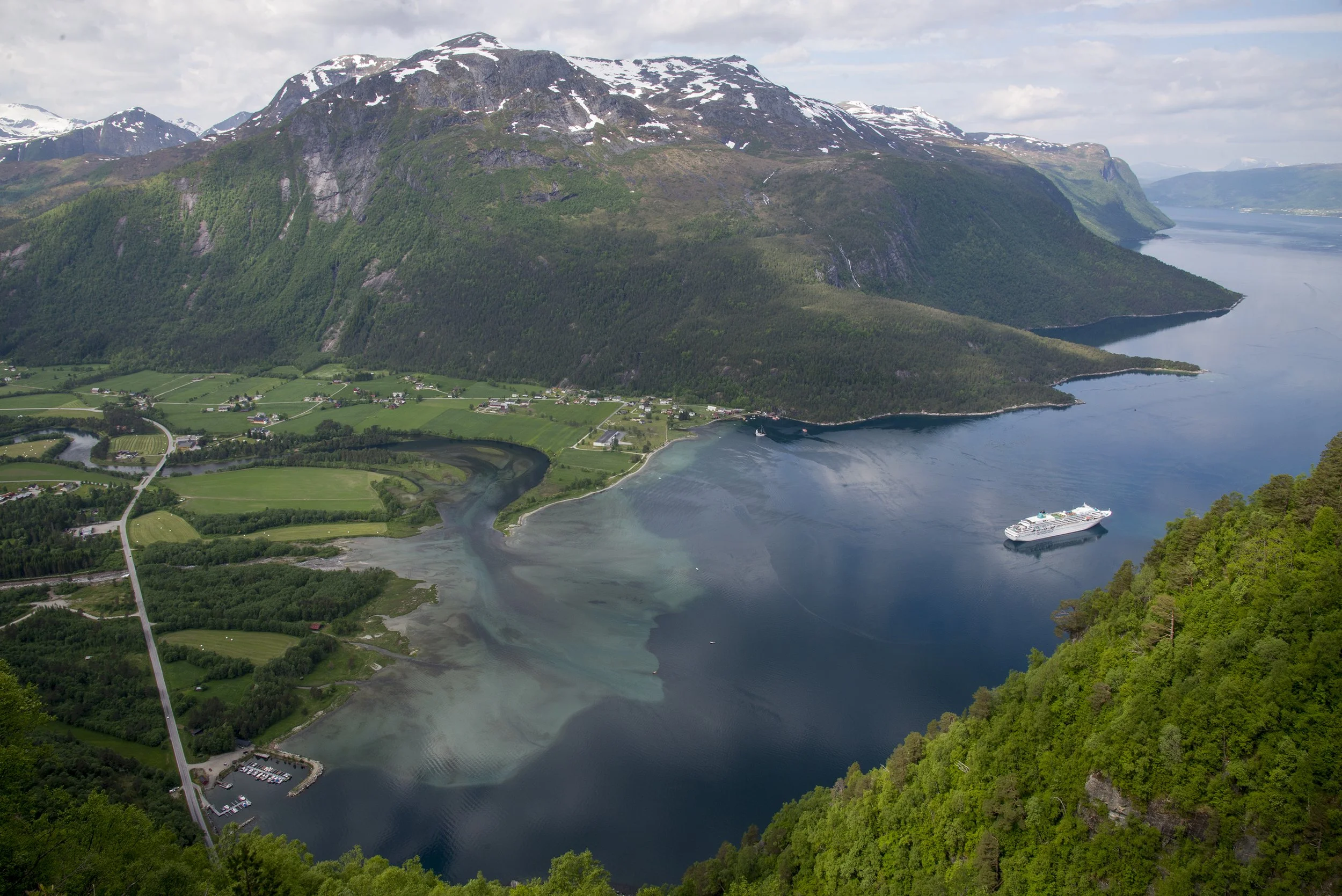 En båt på tur innover Eresfjorden. På bildet ser du grønne jorder og fjellsider, og fjell med snø på toppene. Det er lett overskyet vær.