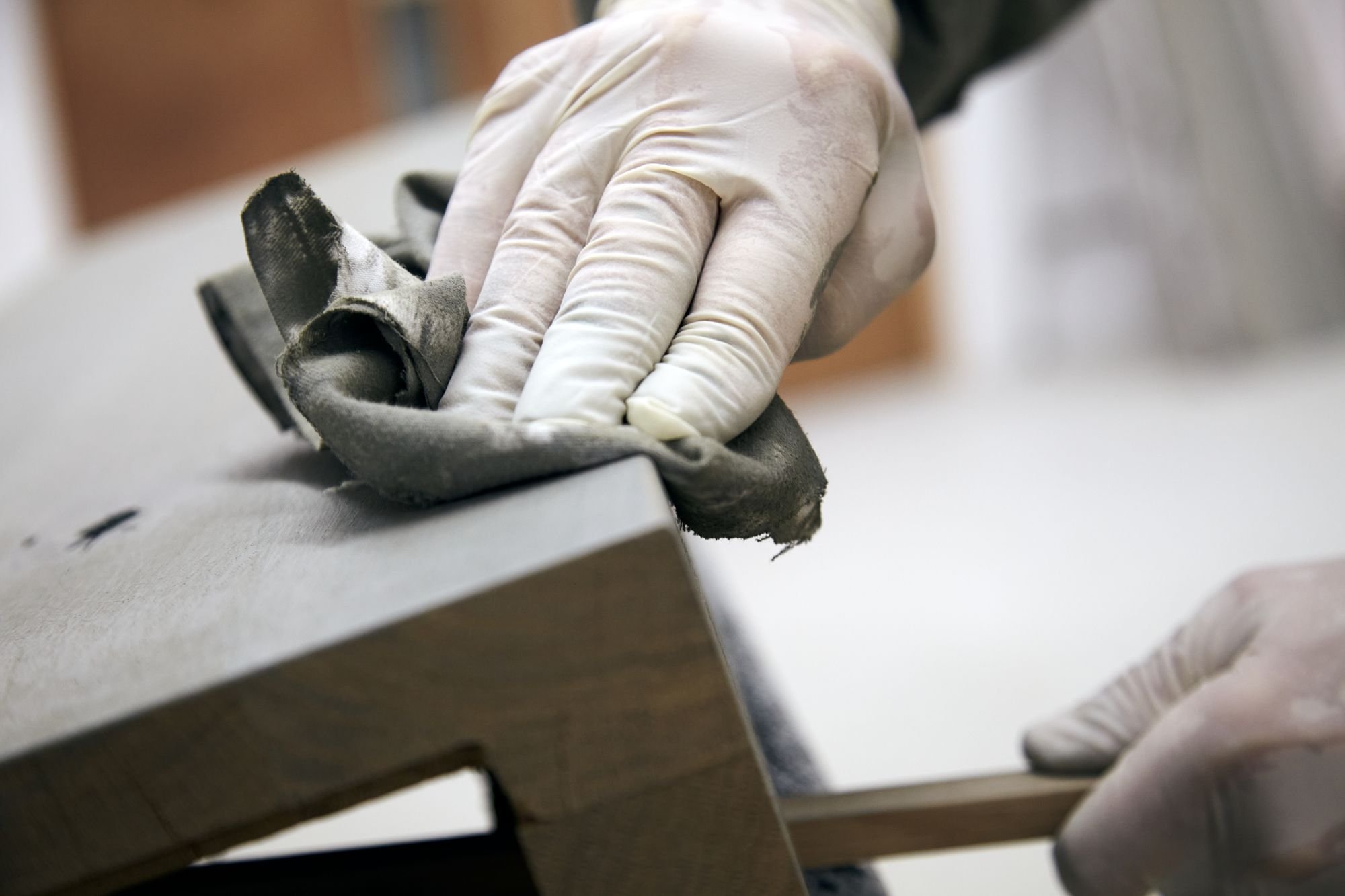 A hand wearing gloves, polishing wood