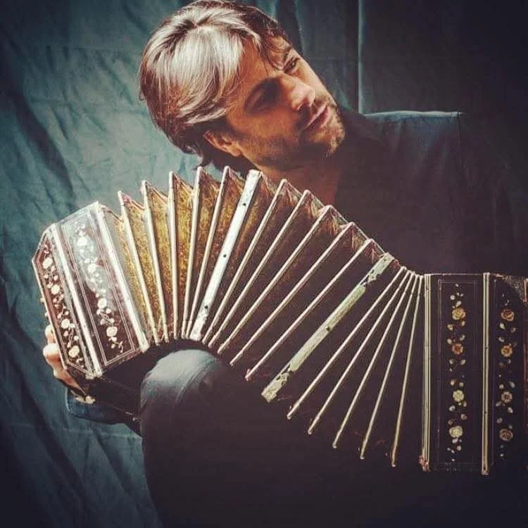 Un uomo con capelli castani e barba tiene un organetto decorato con motivi floreali e dorati.