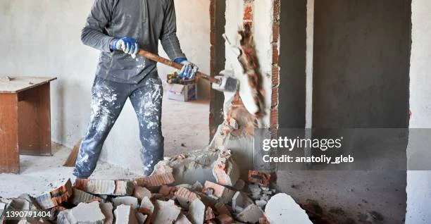 Person demolishing a brick wall with a sledgehammer in a partially renovated room.