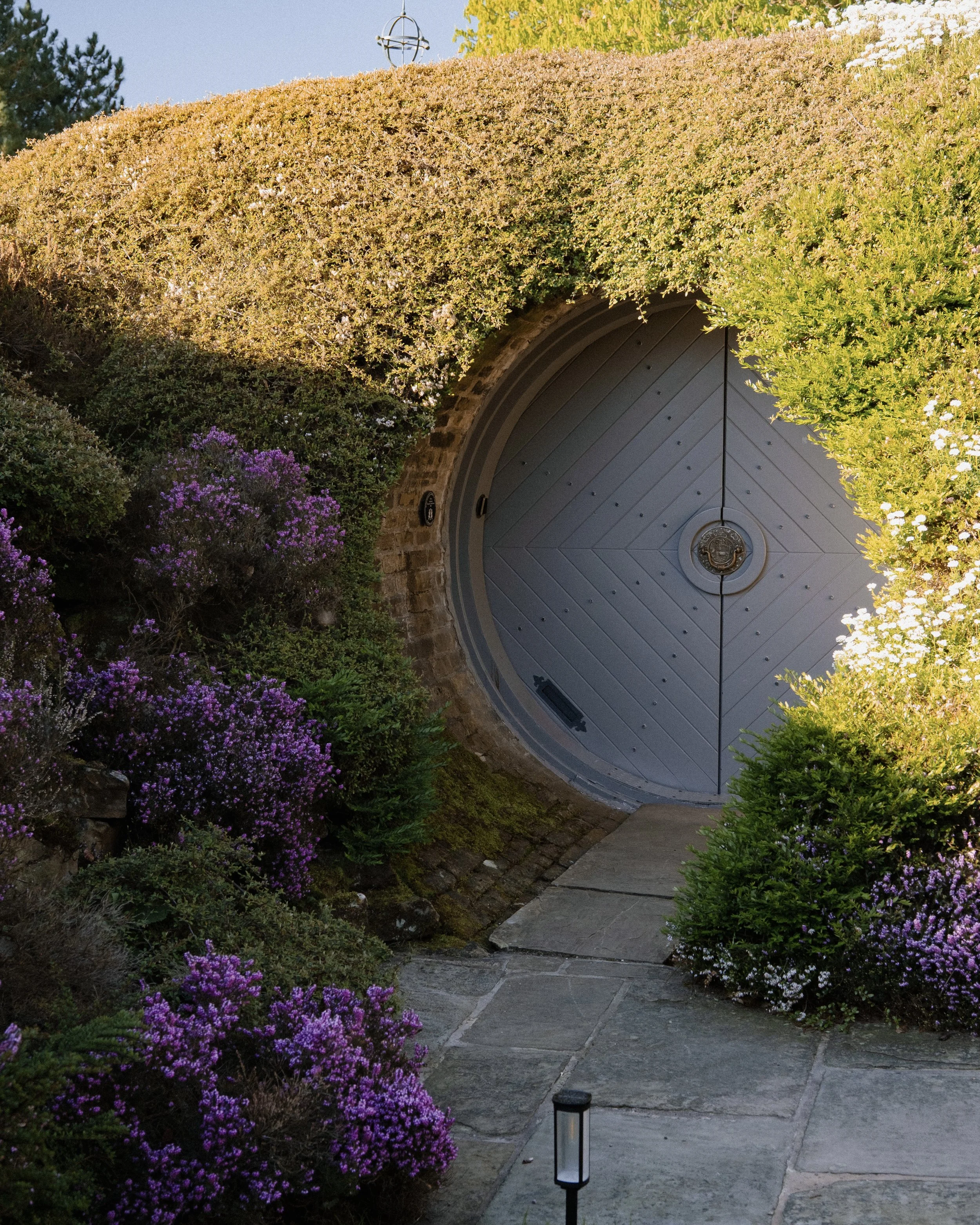 Step through Underhill’s enchanting circular entrance, hidden within the grass-covered hillside and surrounded by colourful planting.