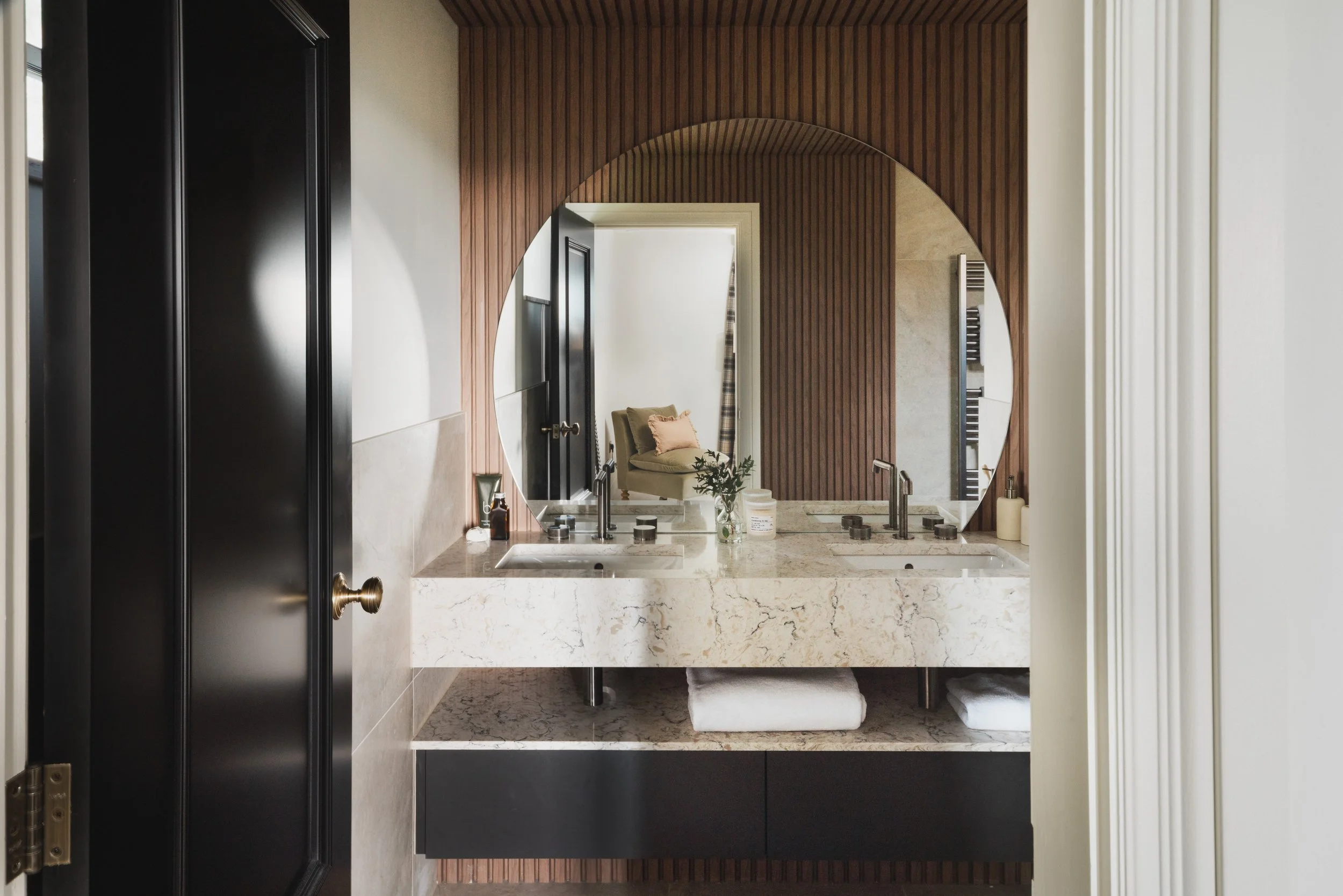 The  statement marble vanity, warm timber detailing and a large circular mirror reflects light softly throughout the space