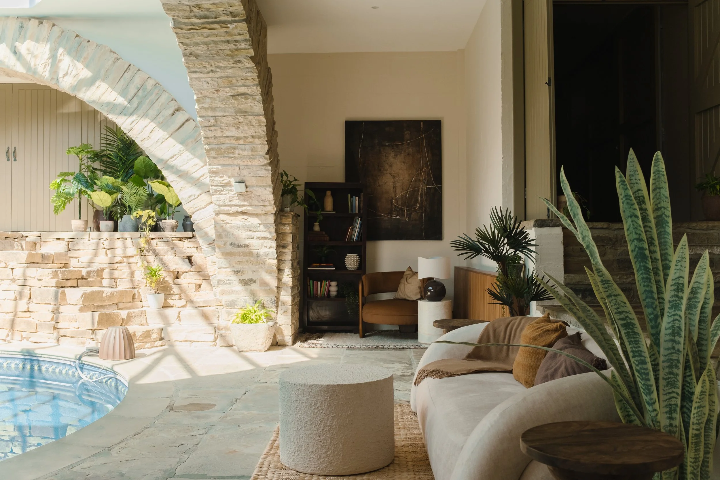 Relax in Underhill’s inviting poolside lounge, with a curved sofa, lush greenery and striking stone arches illuminated by the skylight above.