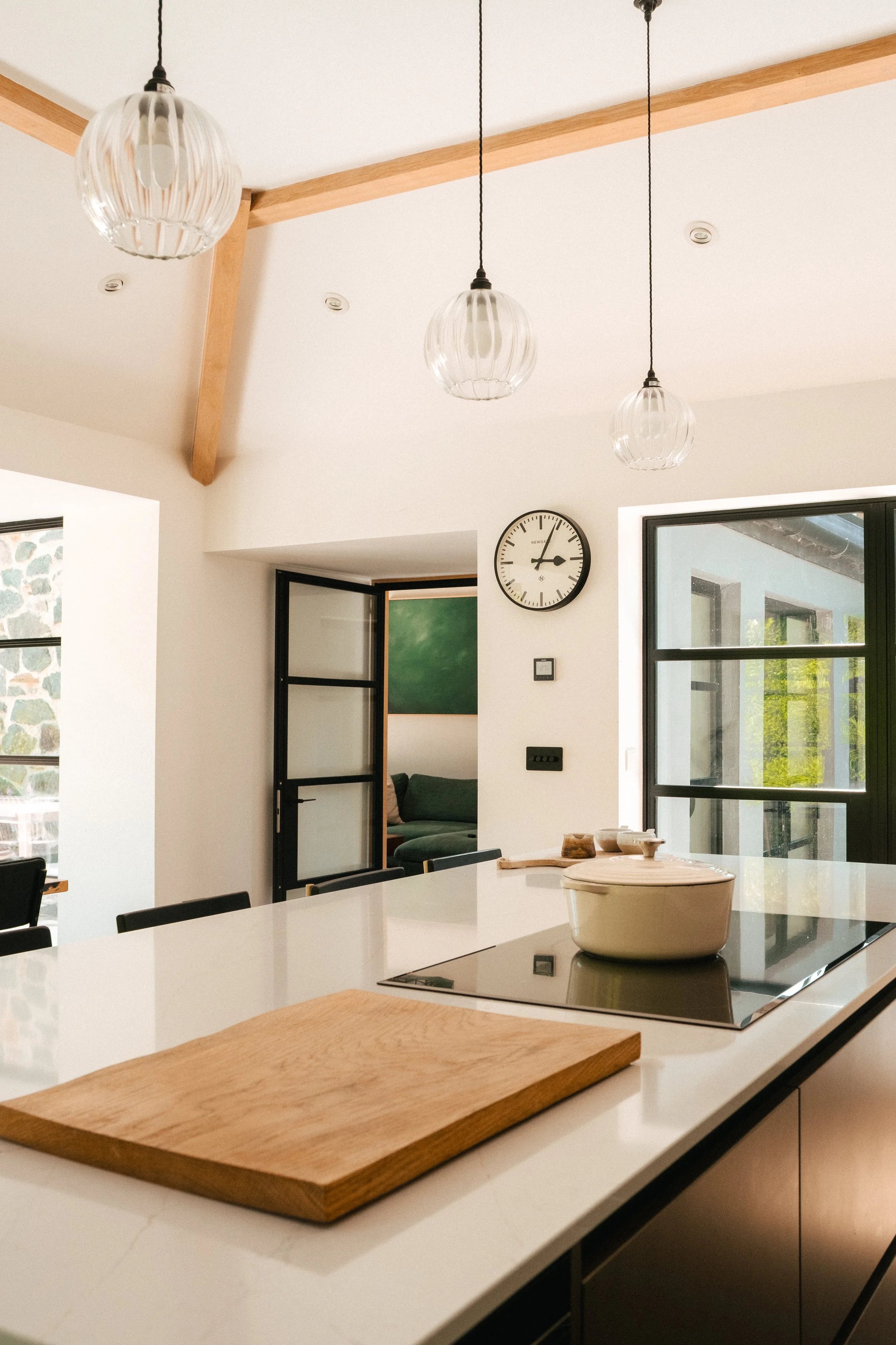 Modern kitchen with white countertops, wooden accents, pendant lights, a wall clock, and a sliding glass door.