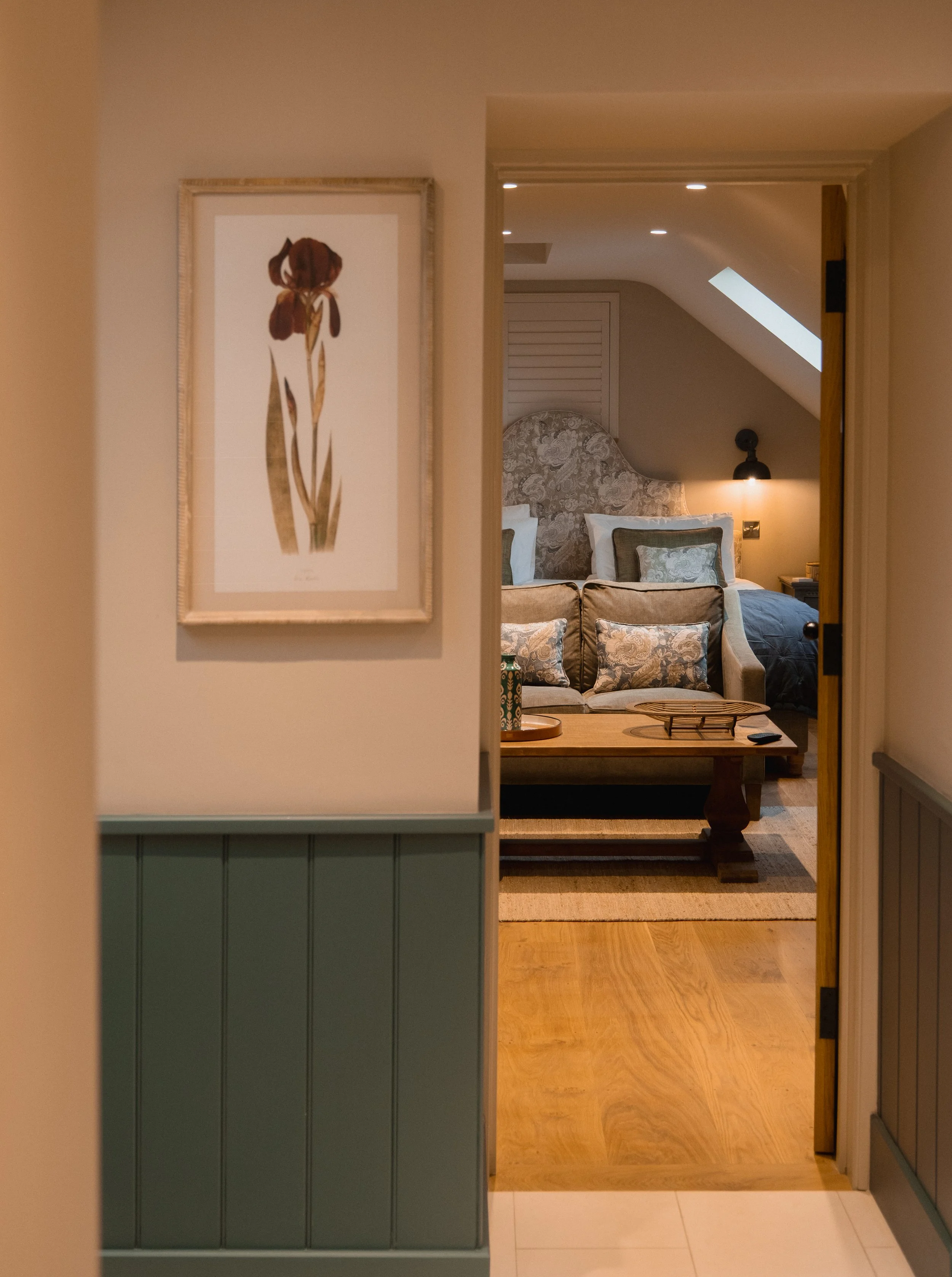 Tucked beneath the sloping eaves, a private seating area and TV create a relaxed extension of the master suite, framed by soft light and warm, natural texture.
