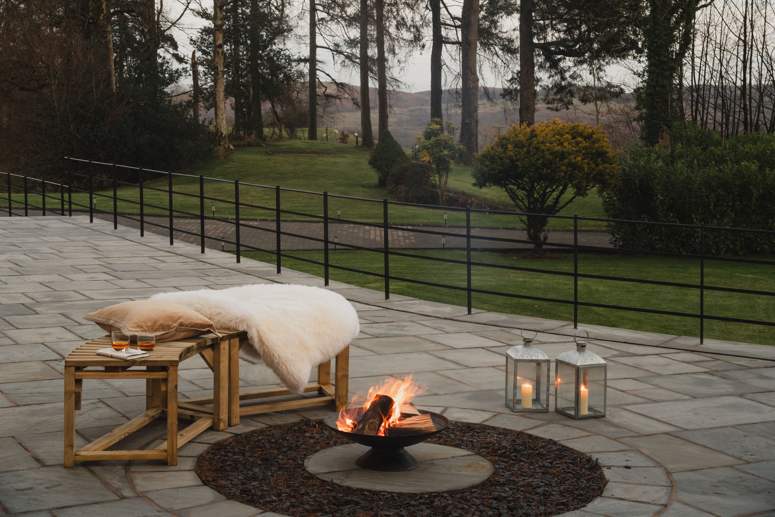 A stone terrace centred around a fire pit, with lantern light and open views across the grounds - made for evenings that stretch on a little longer than planned.