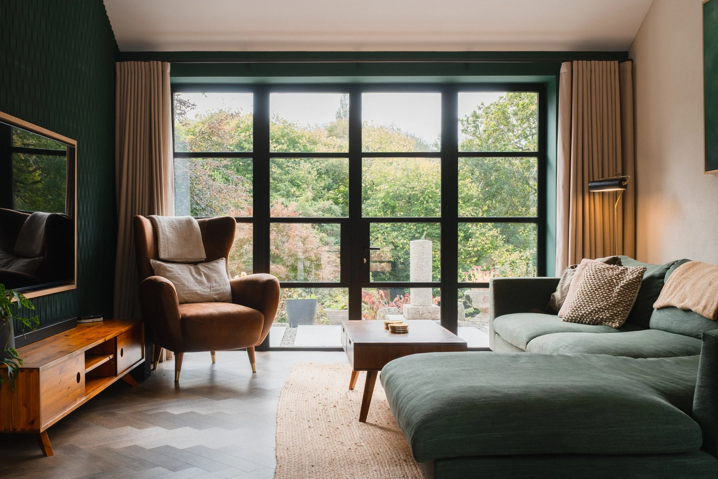 Framed by wide windows and softened by woodland light, the sitting room invites long, unhurried moments of calm. From morning coffee to dusk settling in, this is a space designed simply to be enjoyed.