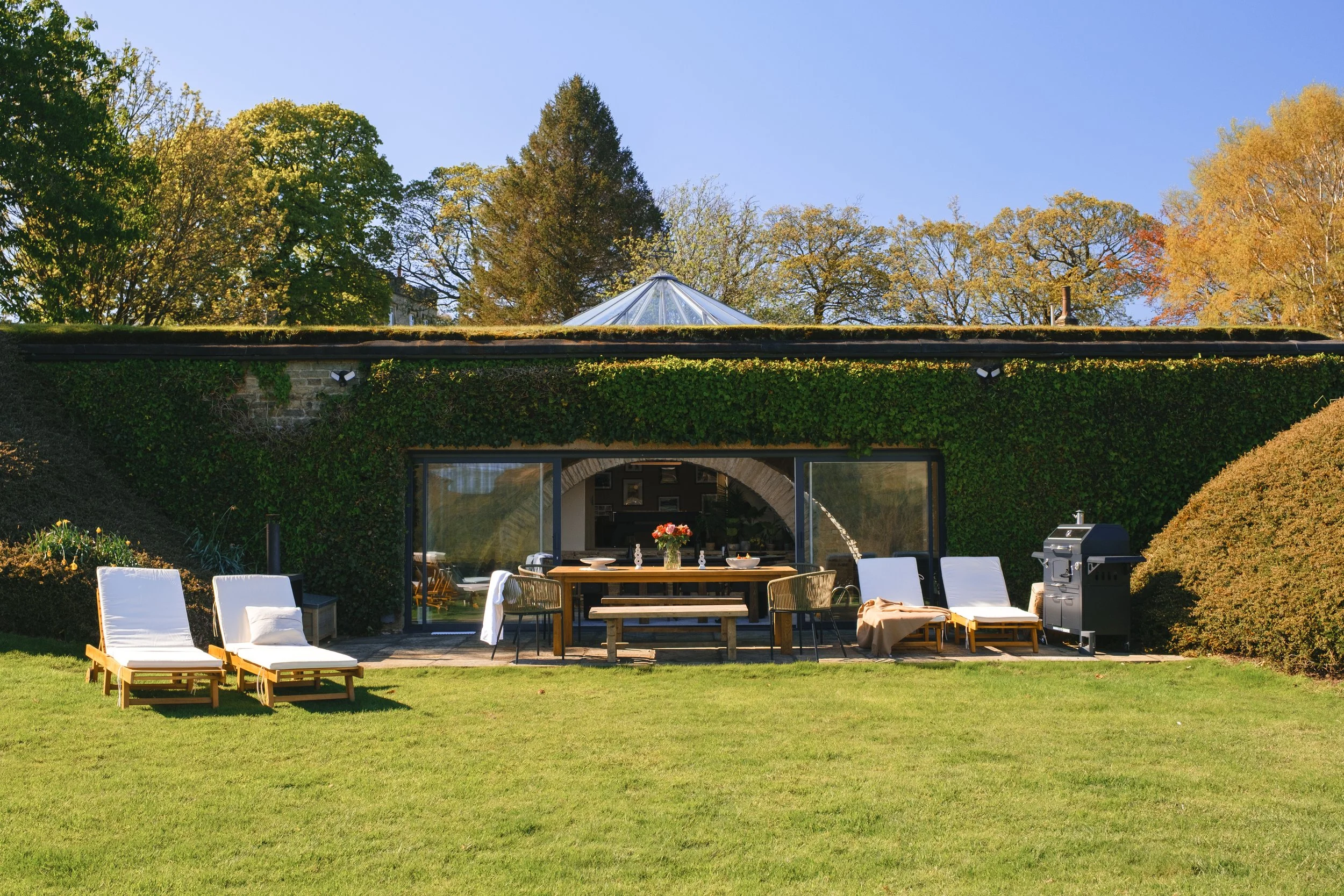 Welcome to Underhill, a unique earth-sheltered retreat with a grass-covered roof, spacious private lawn, outdoor dining area and sun loungers, surrounded by mature trees