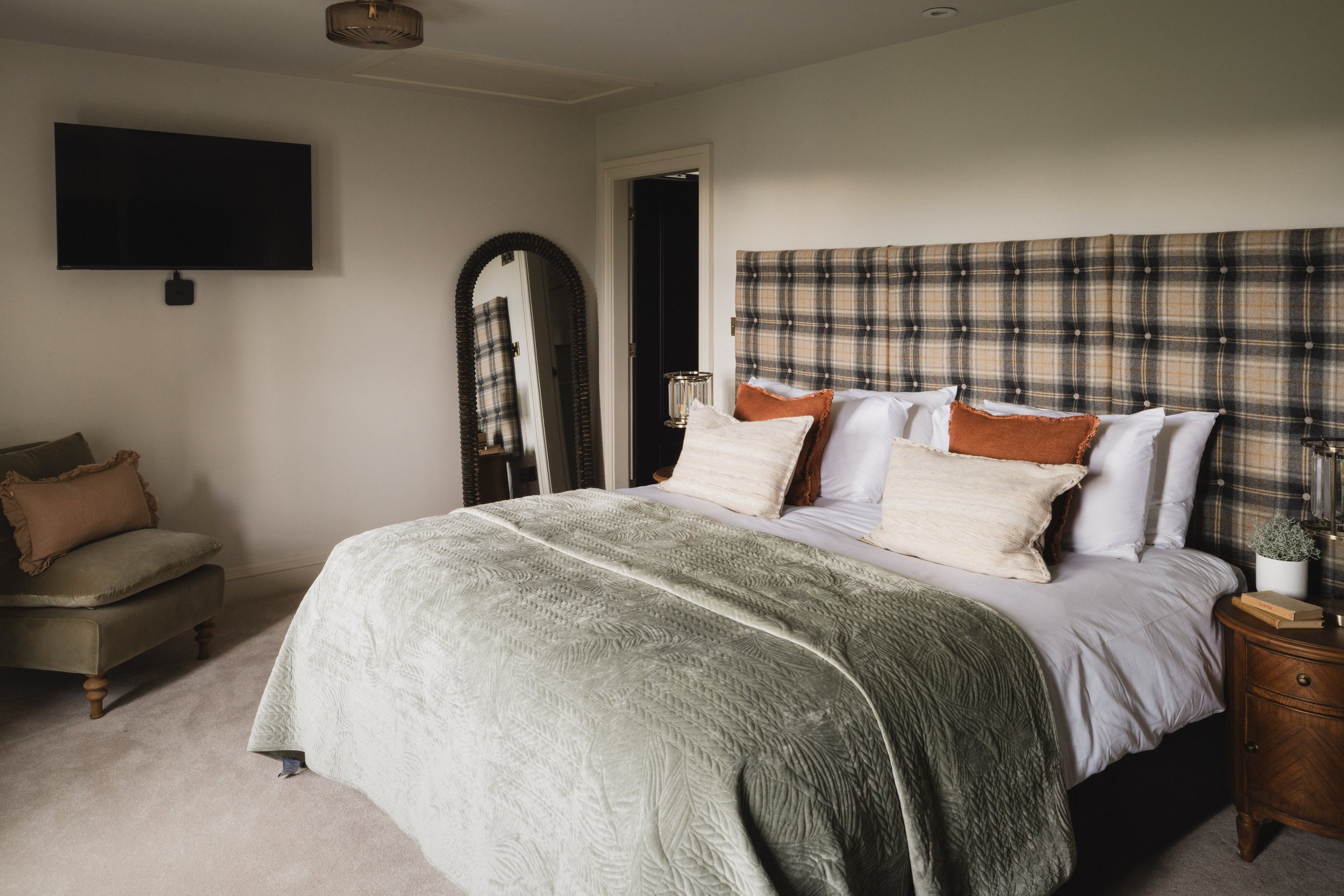 Bedroom one offers a calm and inviting retreat, where a striking tartan headboard, soft layered linens and warm tones create a space made for slow mornings and restful nights.