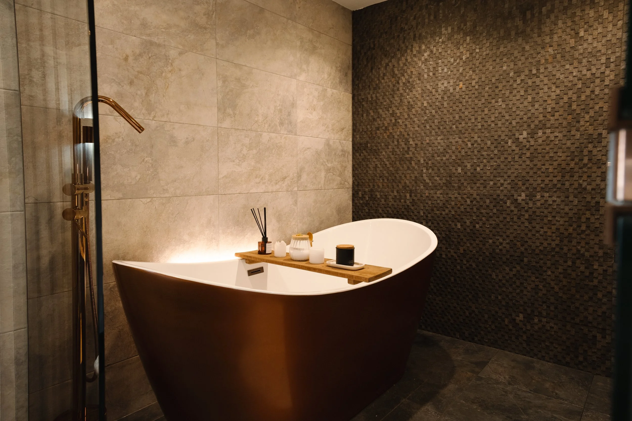 Sink into the sculptural freestanding bath, set against richly textured walls with soft ambient lighting for a deeply relaxing soak.
