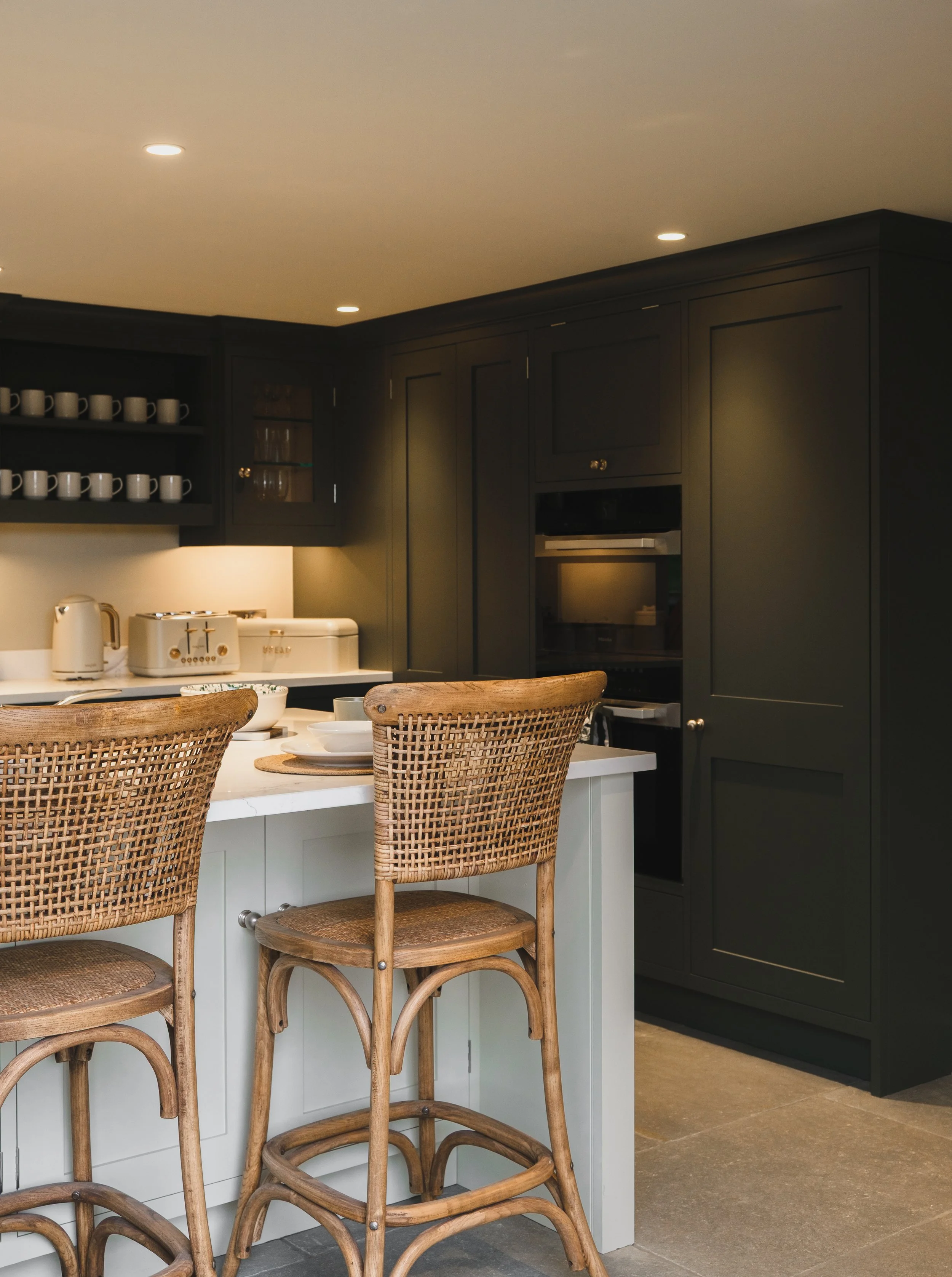 A modern kitchen with black cabinets, a white countertop, and wooden barstools at a kitchen island.