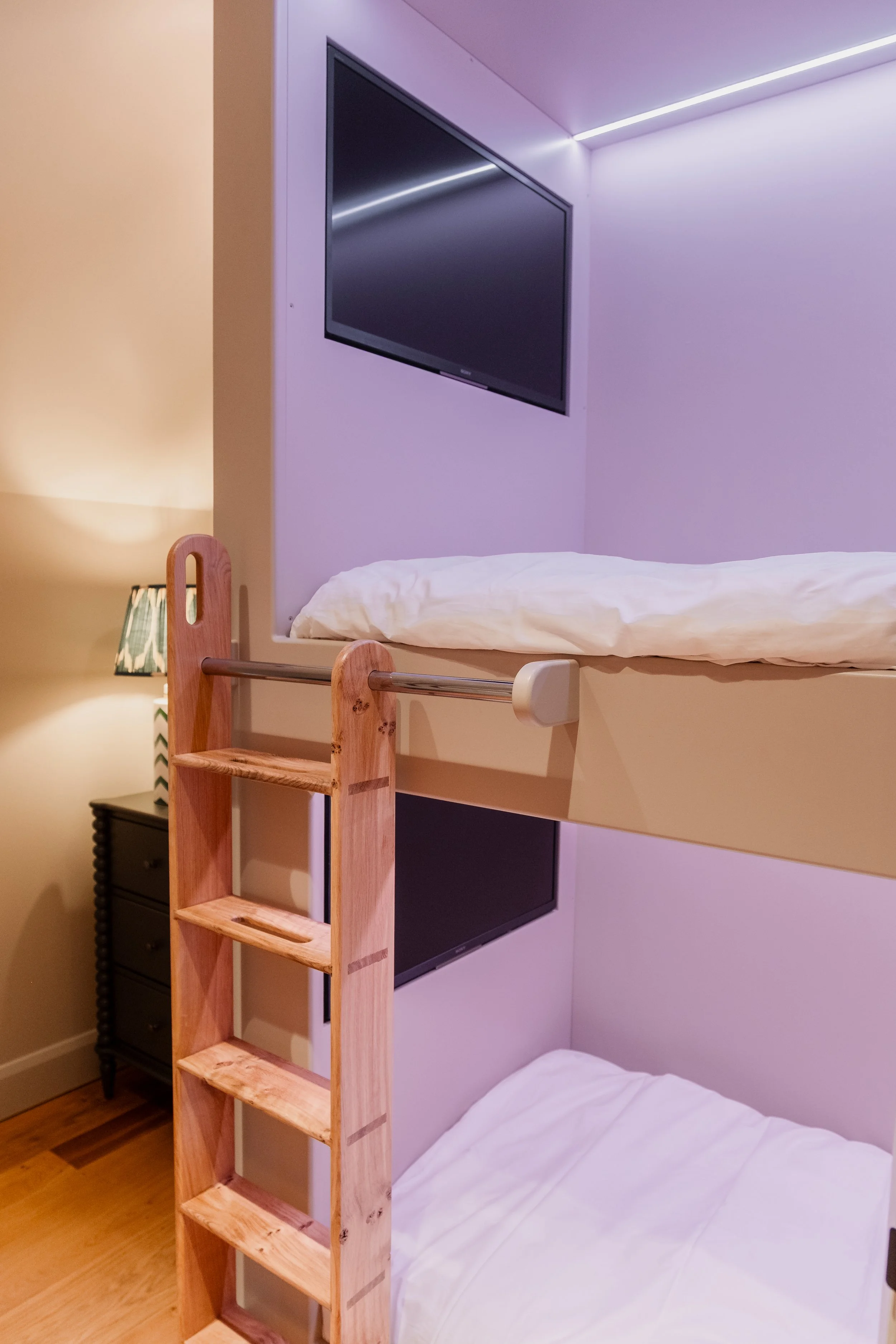 The bunk room brings a playful yet polished energy to the farmhouse, designed as a cosy hideaway for younger guests. Built-in bunks are softly lit with ambient LED lighting, while individual TVs tucked into each nook create private corners.