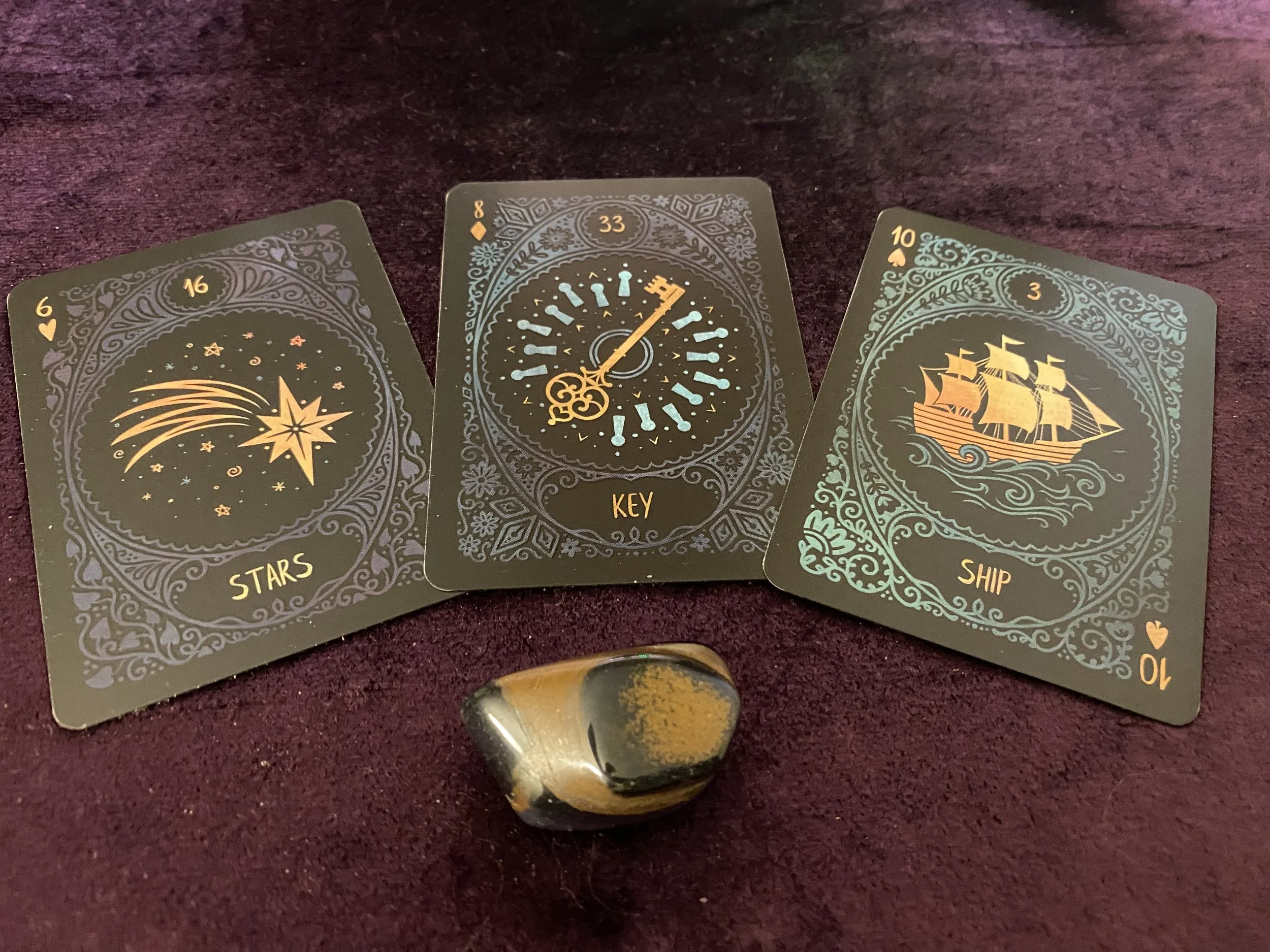 Three tarot cards laid out on a dark surface with a multicolored stone in front of them. The cards are labeled 'Stars,' 'Key,' and 'Ship,' and feature illustrations of a shooting star, a clock, and a sailing ship.