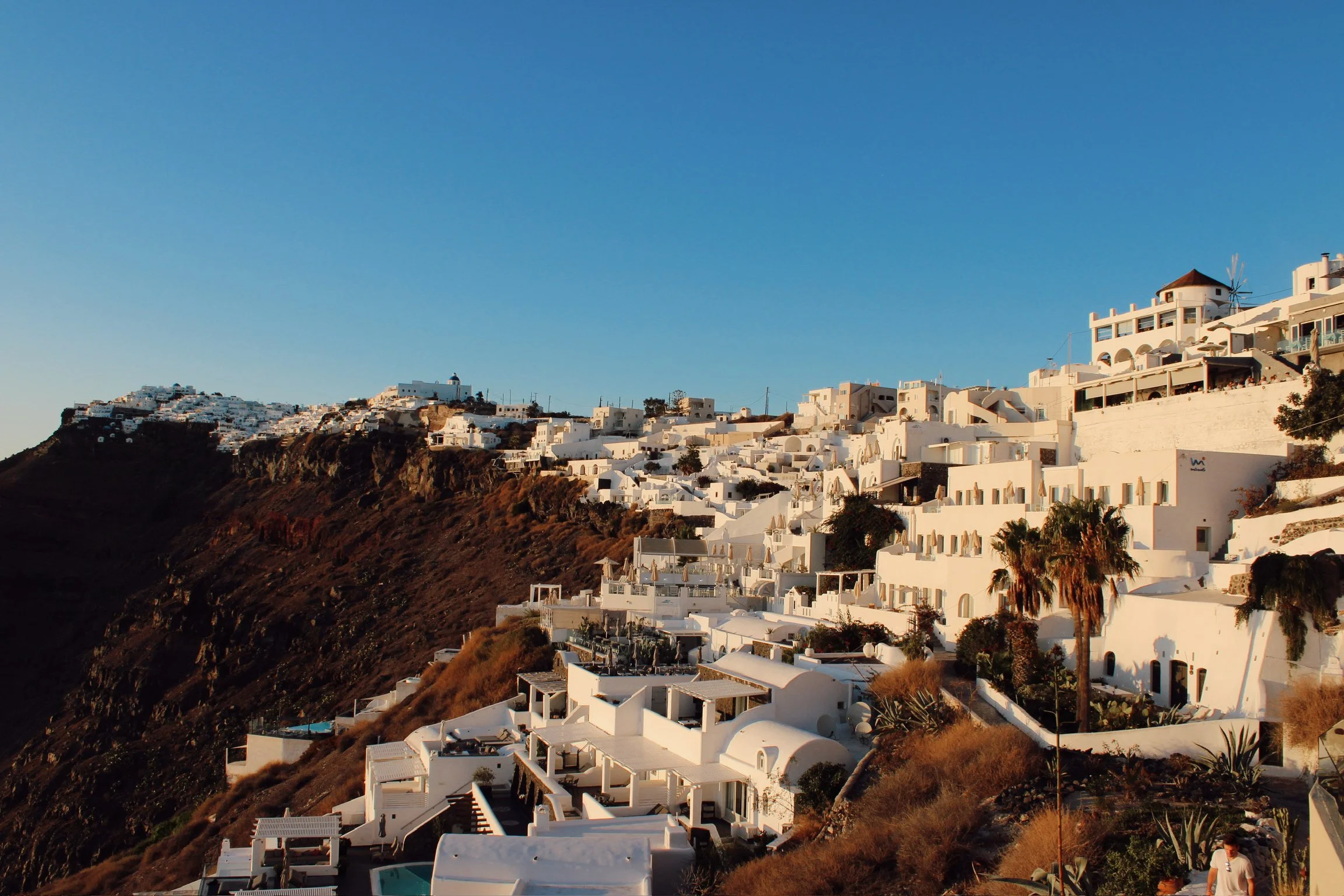 White buildings and villas on a hillside in Santorini with a clear blue sky.
