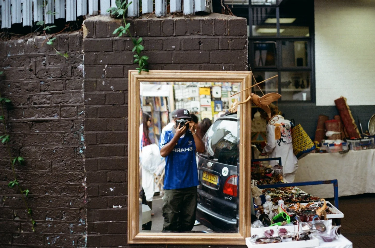 Person taking a photo of their reflection in a mirror at a market stall selling jewelry and accessories.
