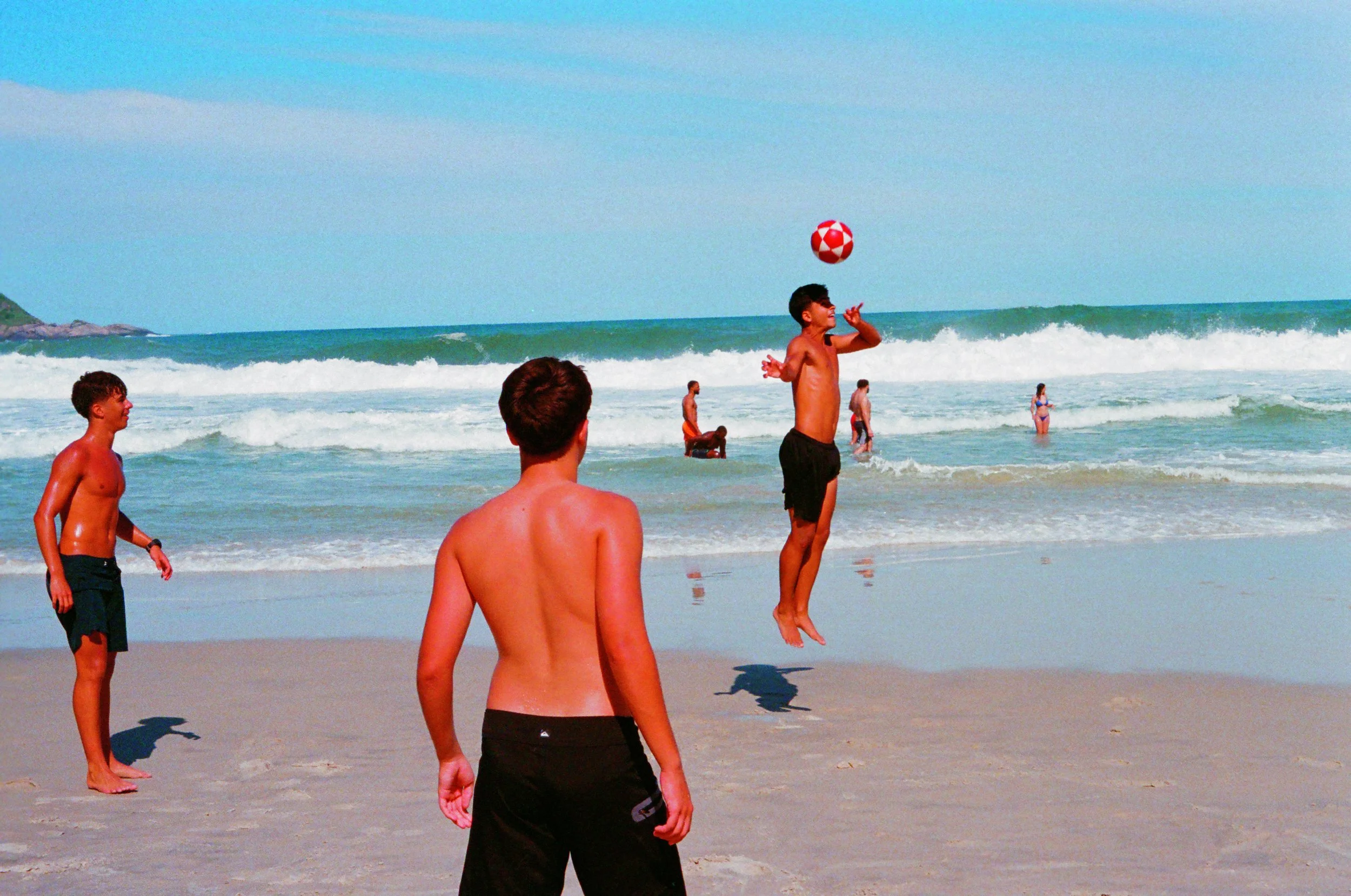 Group of young boys playing football with a ball in the ocean on a sunny day.