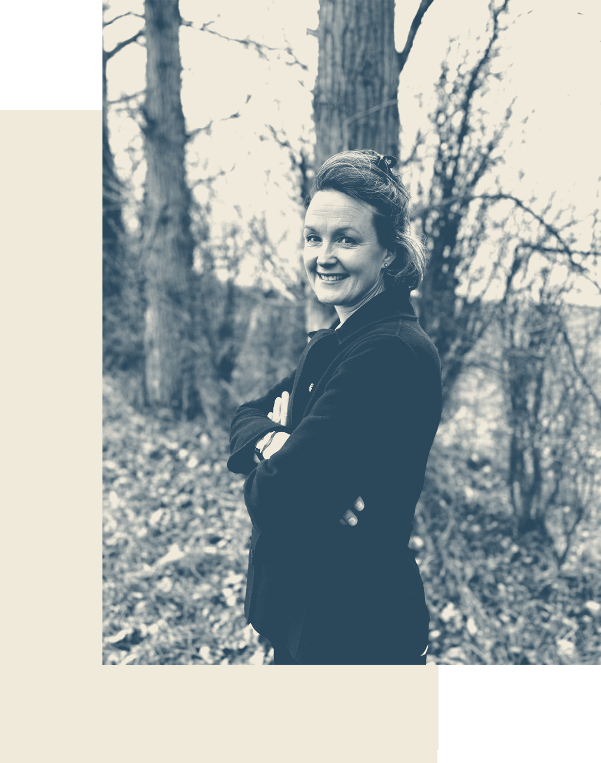 A woman smiling while standing outdoors in front of a tree, with her arms crossed.