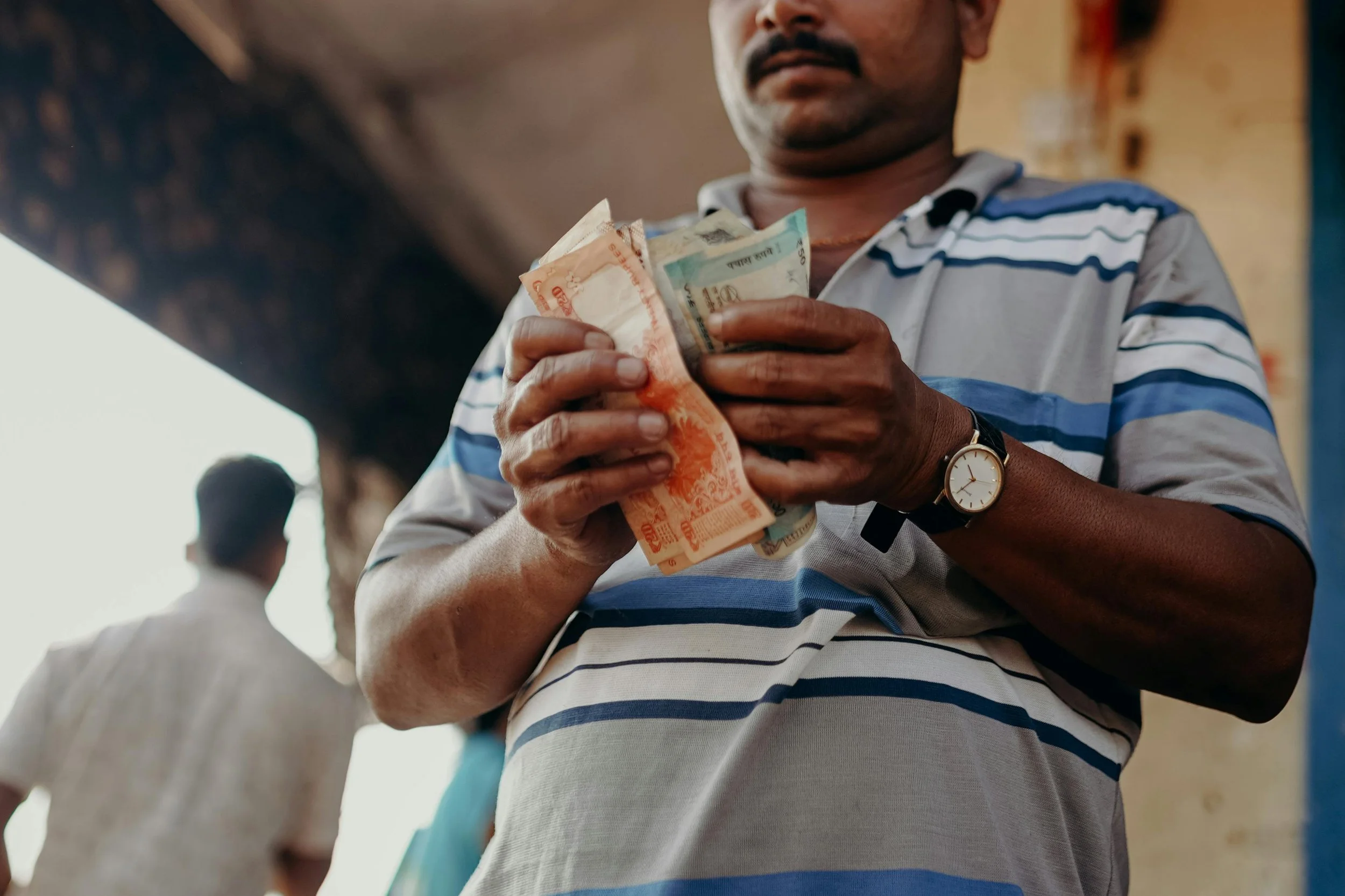 A man wearing a striped polo shirt and a watch is holding a stack of Indian currency notes in his hands.