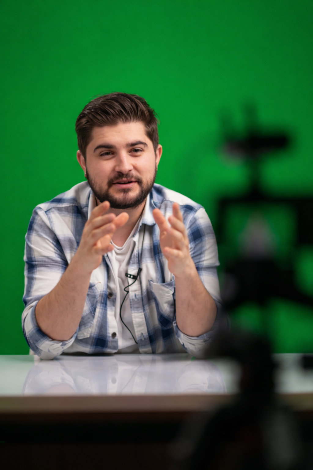 Man with dark hair and beard speaking to a camera in front of a green screen.