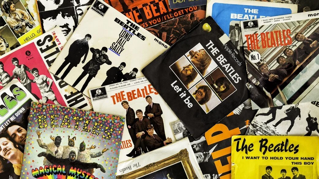A collection of Beatles vinyl records and album covers, including titles like "Let It Be," "Long Tall Sally," and "I Want to Hold Your Hand".