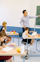 Teacher standing next to chalkboard teaching students in a classroom