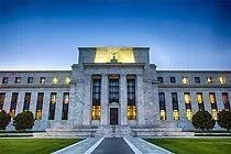 A large government or institutional building with a symmetrical facade, steps leading up to the entrance, and a clock or emblem on top, set against a dusk sky.