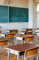 Empty classroom with desks and chairs facing a green chalkboard